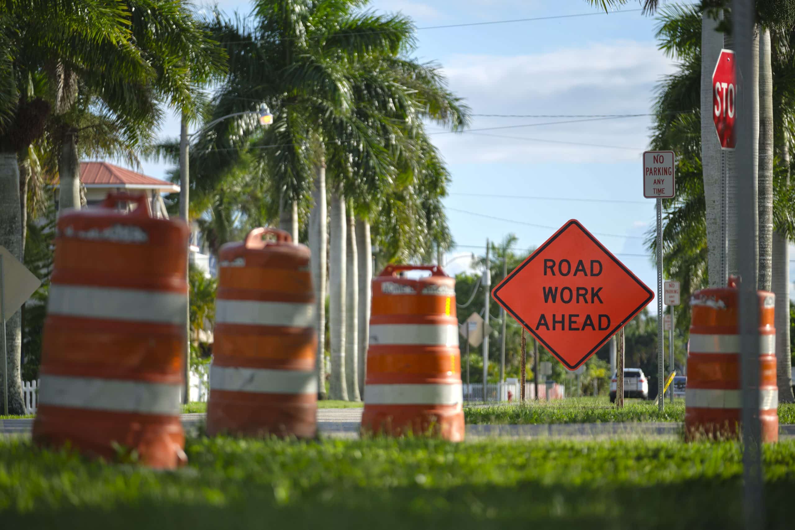 Road work ahead sign and barrier cones on street site as warning to cars about construction and utility works.