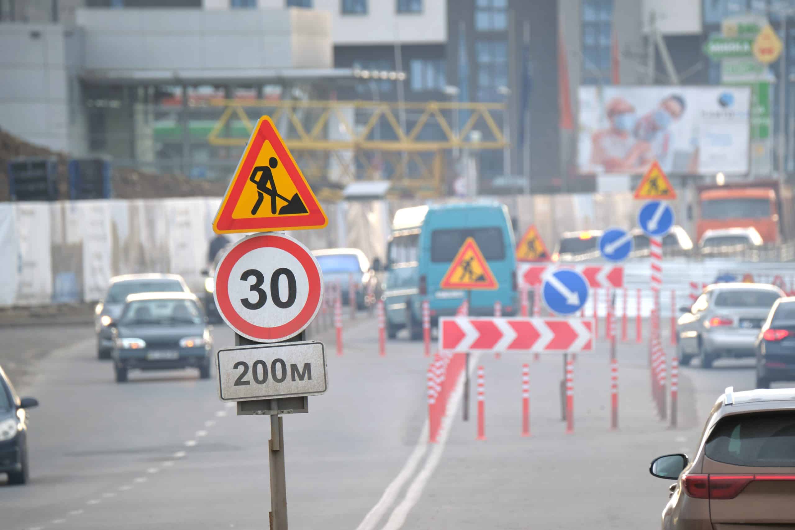 Roadworks warning traffic signs of construction work on city street and slowly moving cars.