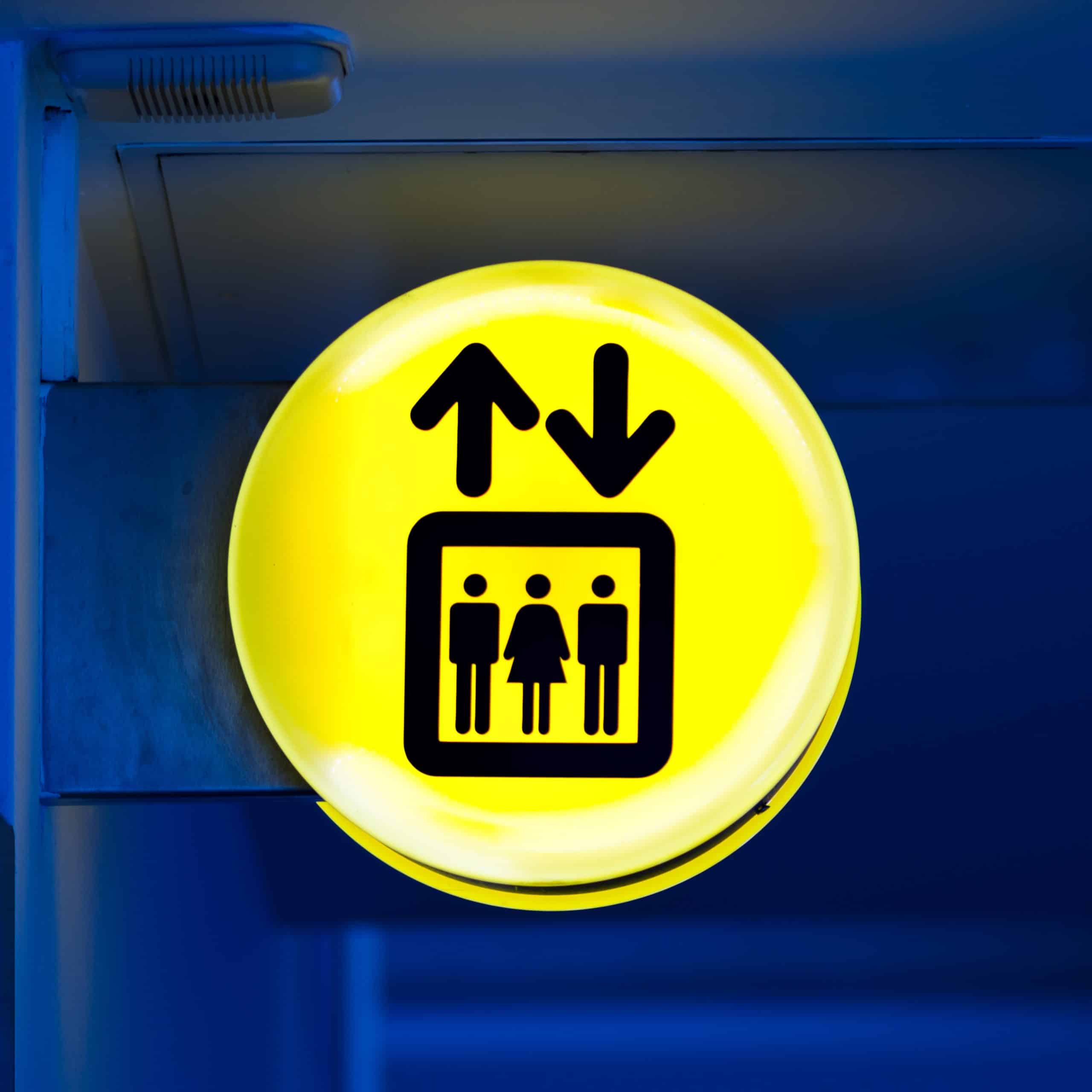 Bright yellow lift or elevator symbol, sign on blue wall background with neon light. Copy space